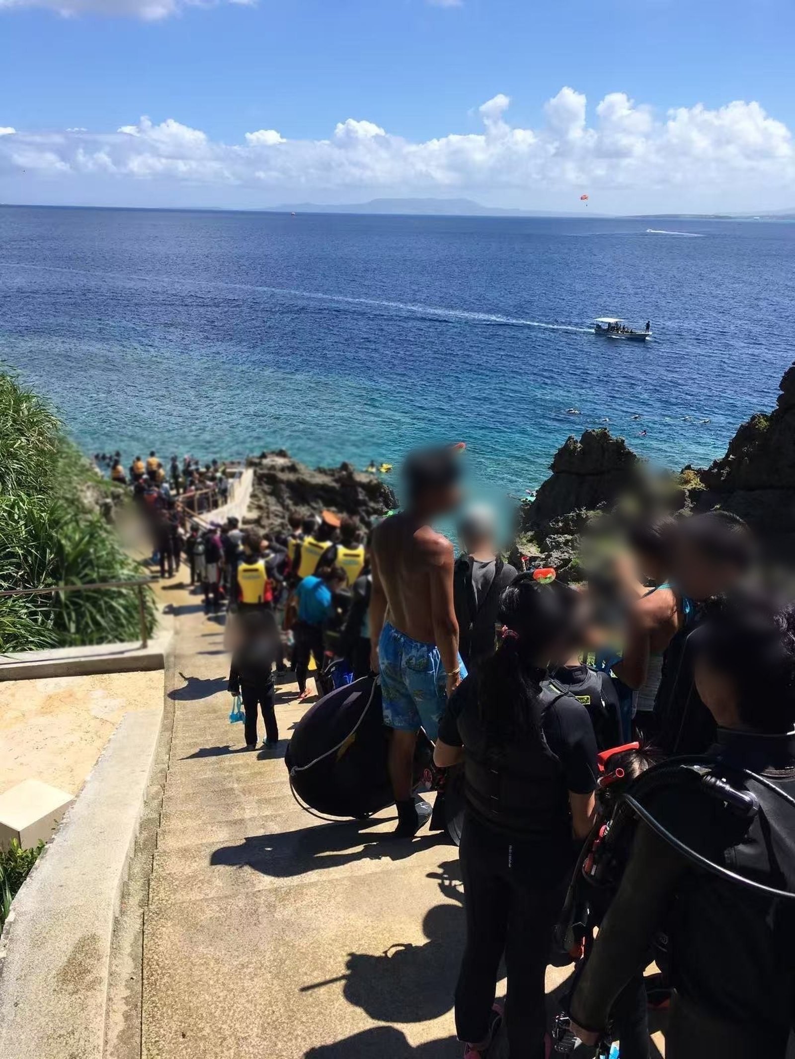 A long queue of snorkelers on the stairway down to the Blue Cave entry point, with open ocean behind